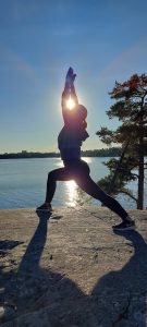 Nainen joogaa kallion päällä. Taustalla on meri ja auringonlasku