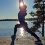 Nainen joogaa kallion päällä. Taustalla on meri ja auringonlasku
